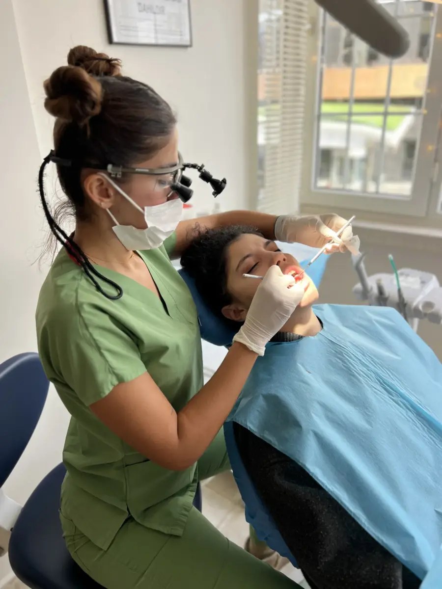 Our head dentist, Ayşenur Kayimbaşıoğlu, examines her patient using her dental loupe and hand instruments while seated in the dentist's chair.