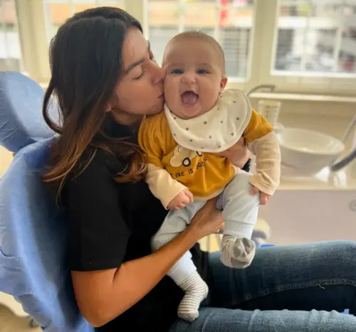 Our head dentist Dr Ayşenur Kayımbaşıoğlu smiles together as she holds a newborn baby before examining her in our AuraDent clinic room.