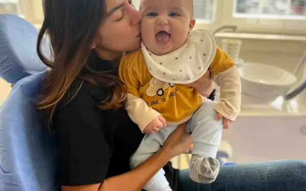 Baş hekimimiz Dr. Ayşenur Kayımbaşıoğlu, AuraDent Klinik odamızda yeni doğmuş bir bebeği muayene etmeden önce elinde tutarken birlikte gülümsüyorlar.